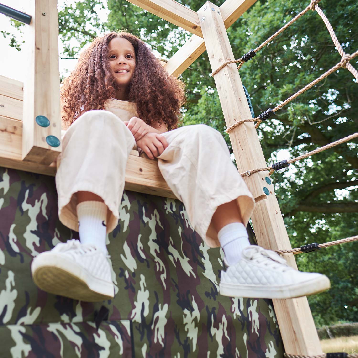 A smiling girl sitting on the top platform of Plum Play's Wooden Climbing Cube