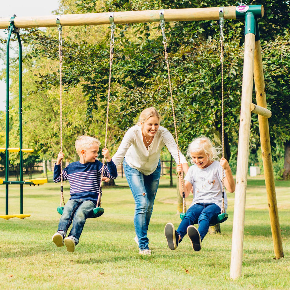Mom pushing her children while they sit in the swings of Plum Play's Colobus Wooden Swing Set