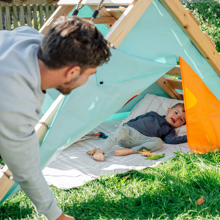 Dad looking at his son lying in the den under the frame of Plum's My First Wooden Playcentre