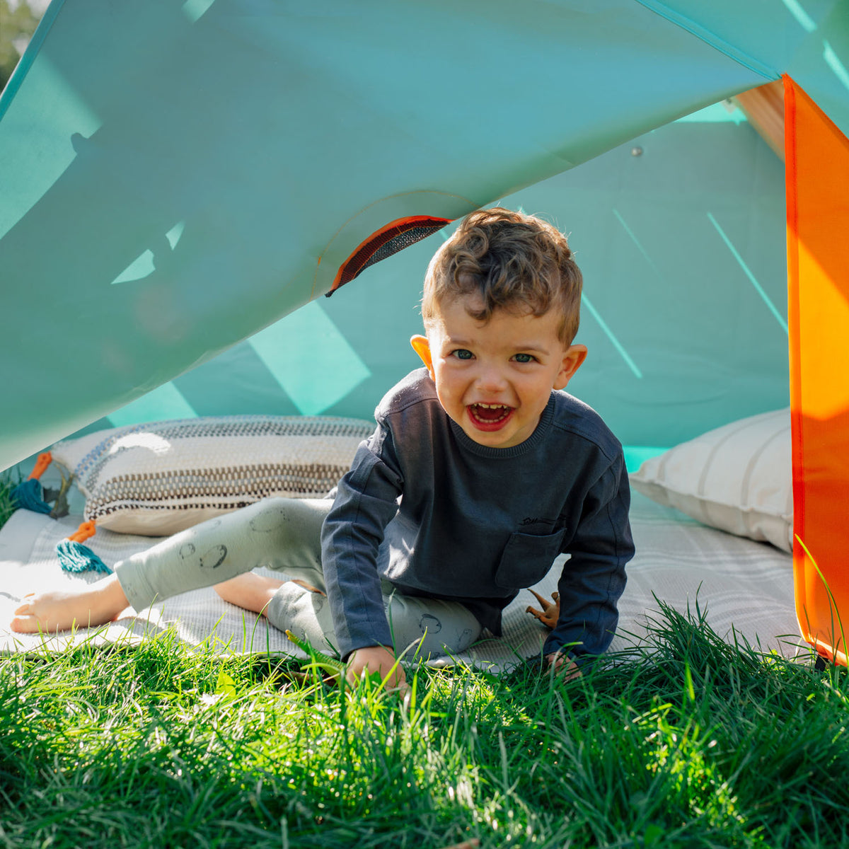 A toddler smiling while sitting under the den of Plum's My First Wooden Playcentre