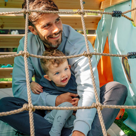 Dad and son sitting in the den of Plum Play's My First Wooden Playcentre