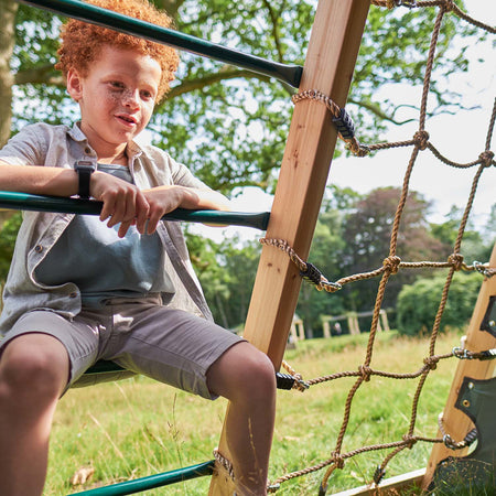 Young boy sitting on the rungs of ladder of Plum Play's Climbing Pyramid Wooden Climbing Frame