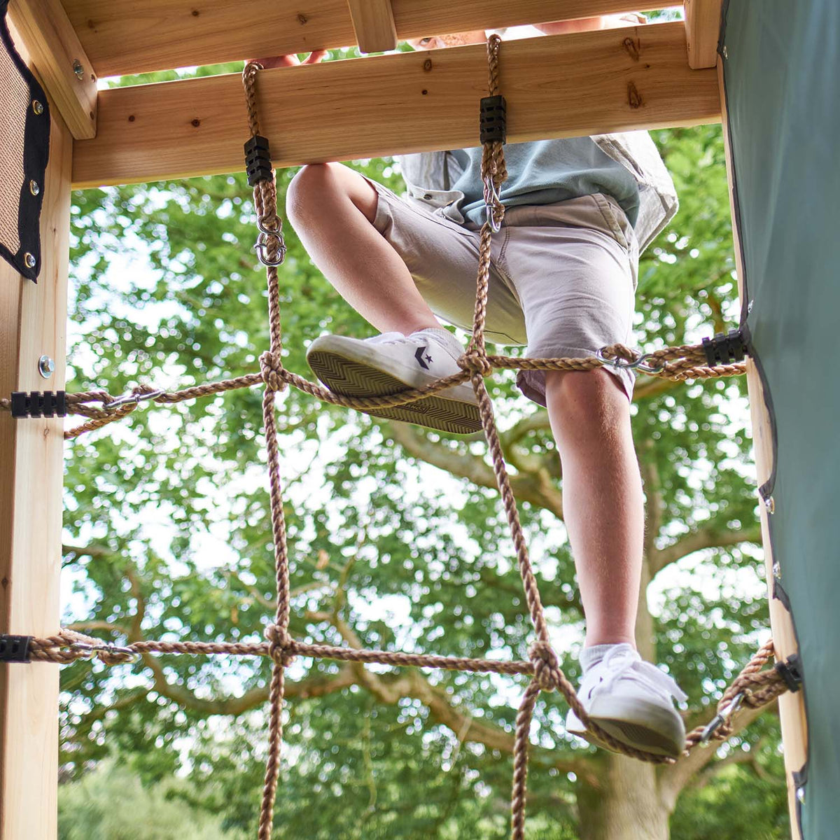 Feet of a child climbing on the cargo net of Plum Play's Climbing Pyramid Wooden Climbing Frame
