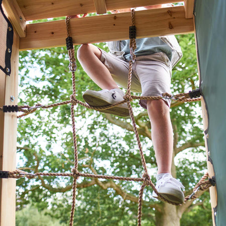 Feet of a child climbing on the cargo net of Plum Play's Climbing Pyramid Wooden Climbing Frame