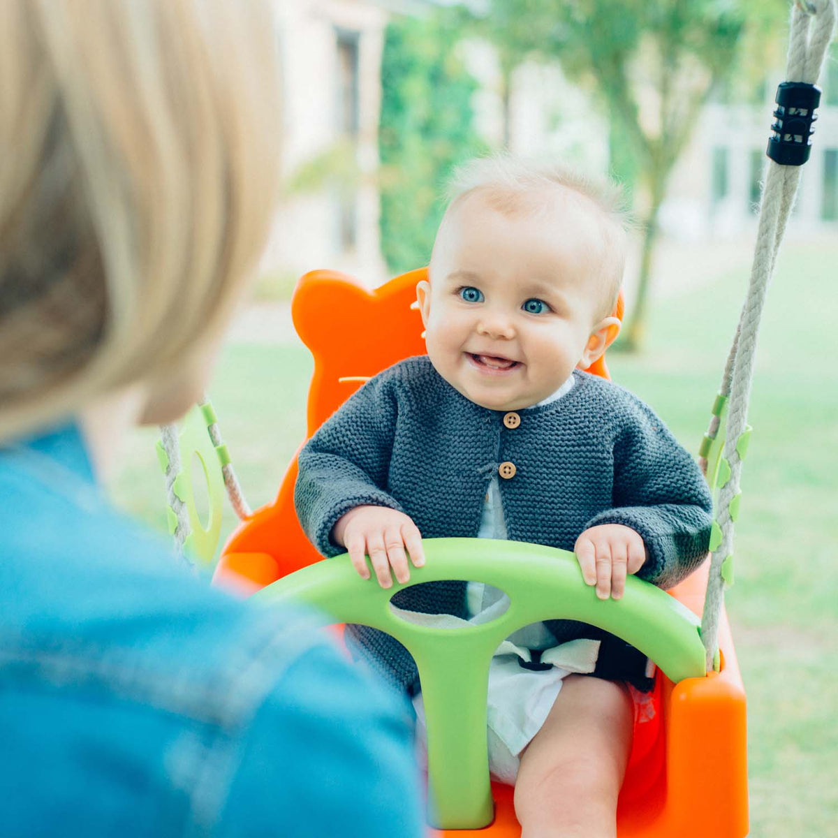 A baby smiling back while sitting in the baby swing of Plum Play's 3-in-1 Wooden Growing Swing Set