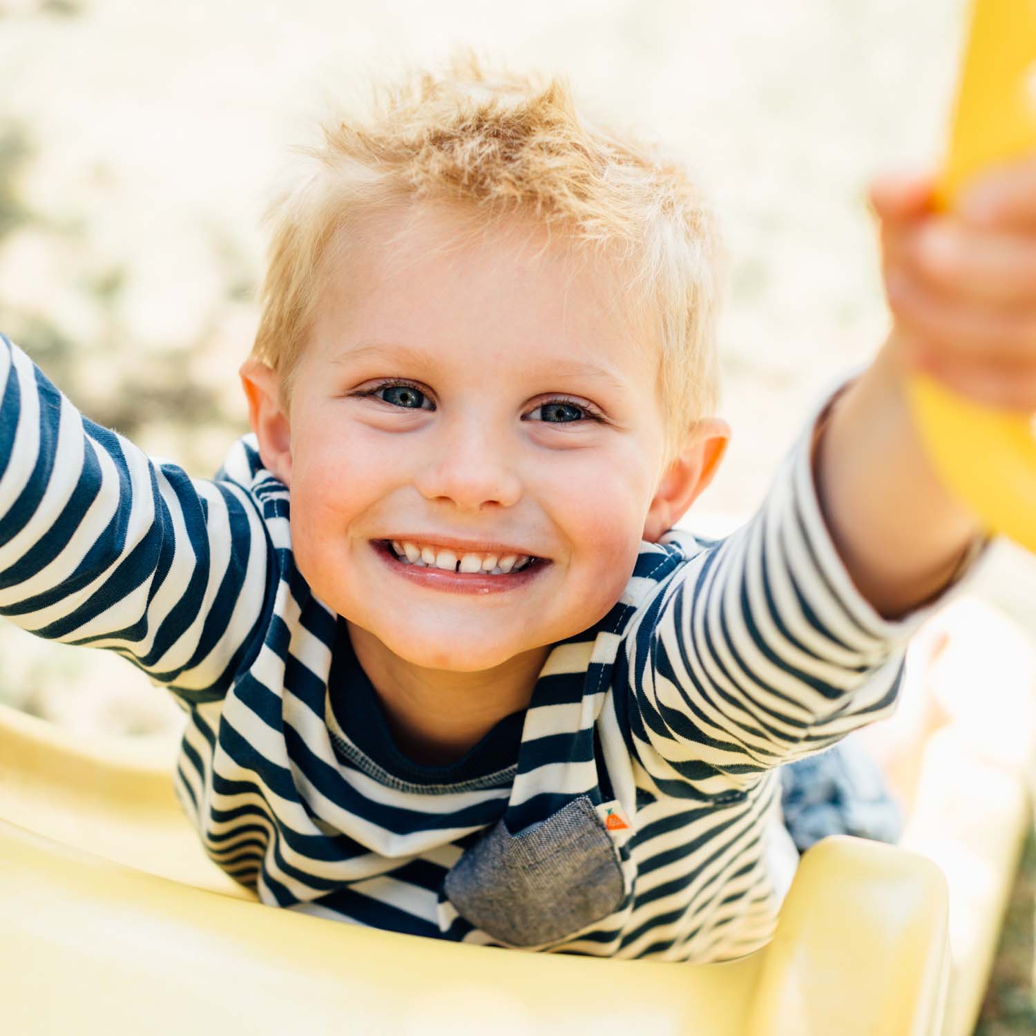 A young boy smiling while lying on the slide of Plum Play's Toddlers Tower Wooden Climbing Frame