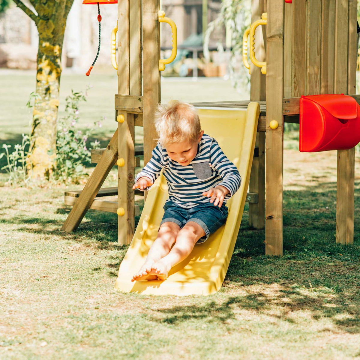 A young boy enjoying the slide in Plum Play's Toddlers Tower Wooden Climbing Frame