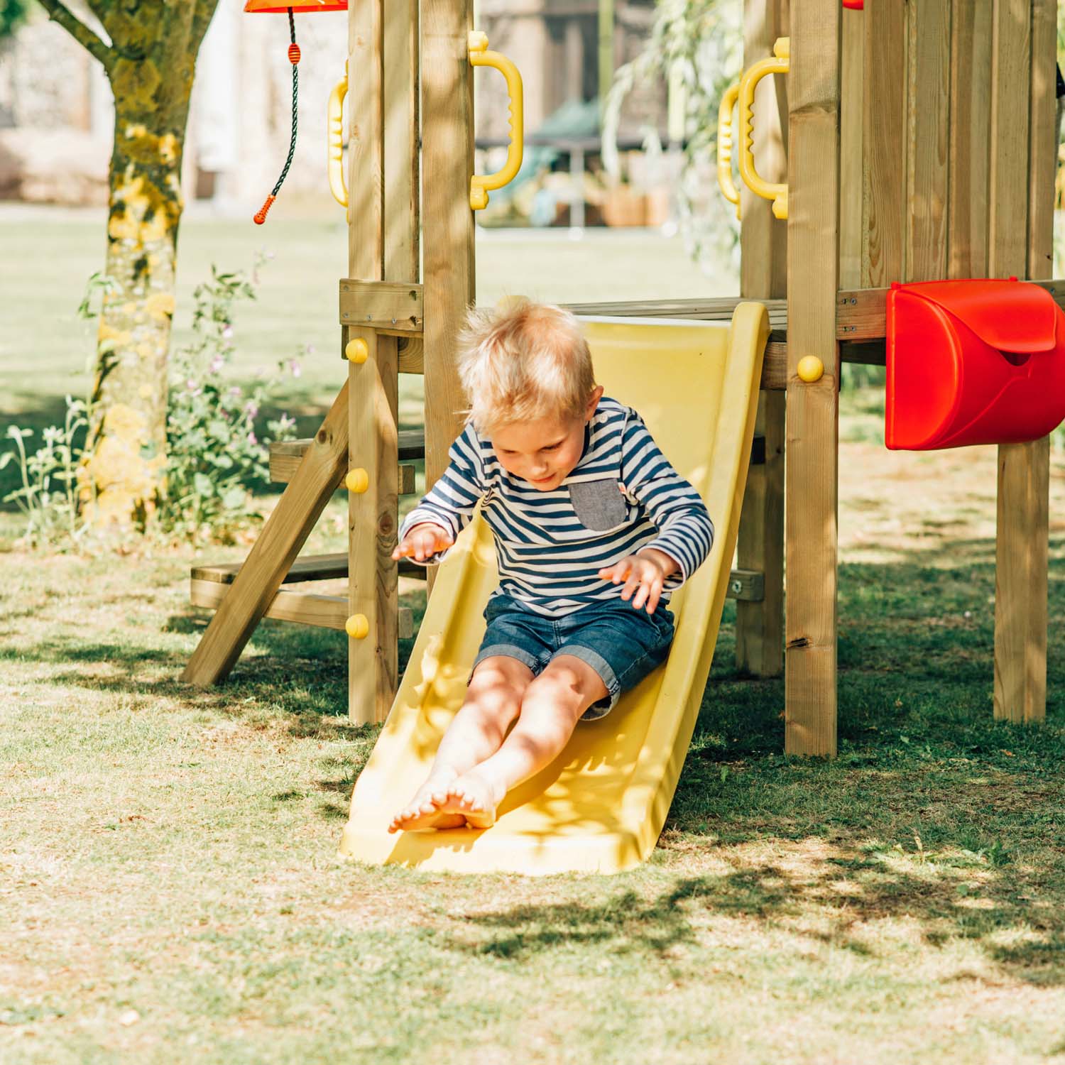 A young boy enjoying the slide in Plum Play's Toddlers Tower Wooden Climbing Frame