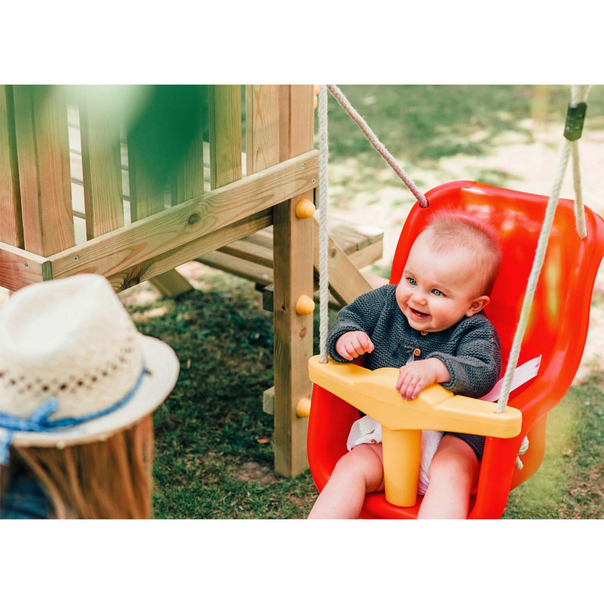An infant sitting on the baby swing of Plum Play's Toddlers Tower Climbing Frame while smiling to her mother