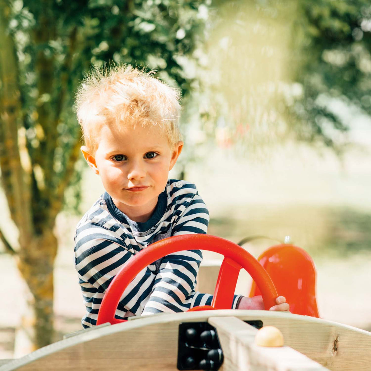 A young boy holding the steering wheel accessory in Plum Play's Toddlers Tower Wooden Climbing Frame