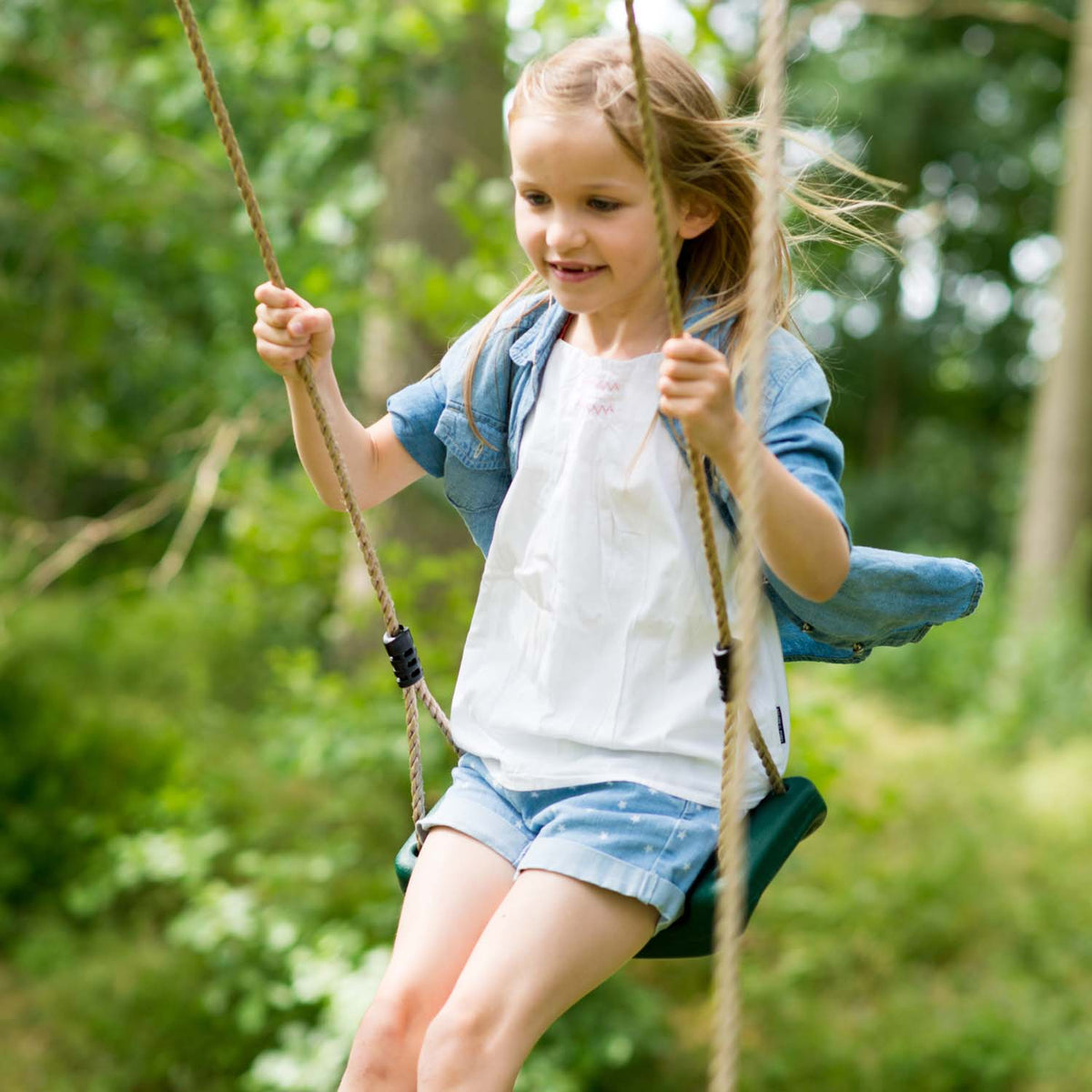 A girl having fun swinging in Plum Play's Woolly Monkey II Wooden Swing Set