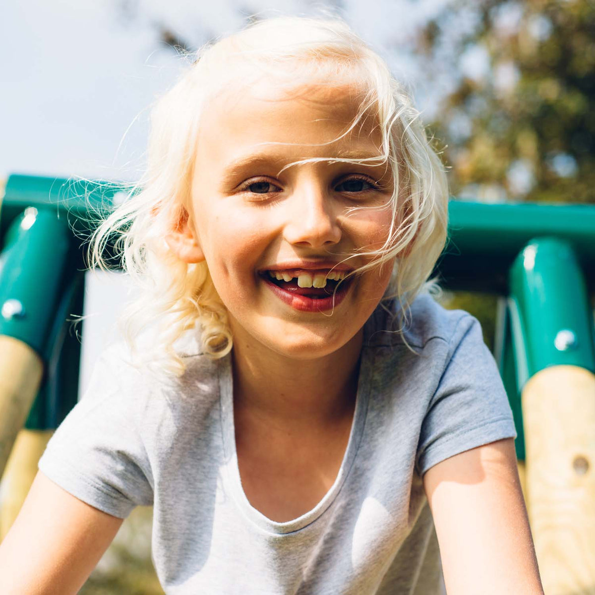 A girl smiling while climbing in the Plum Play's Woolly Monkey II Wooden Swing Set
