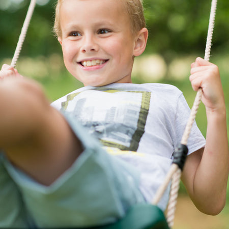 A smiling boy while swinging in Plum Play's Wooden Double Swing Set