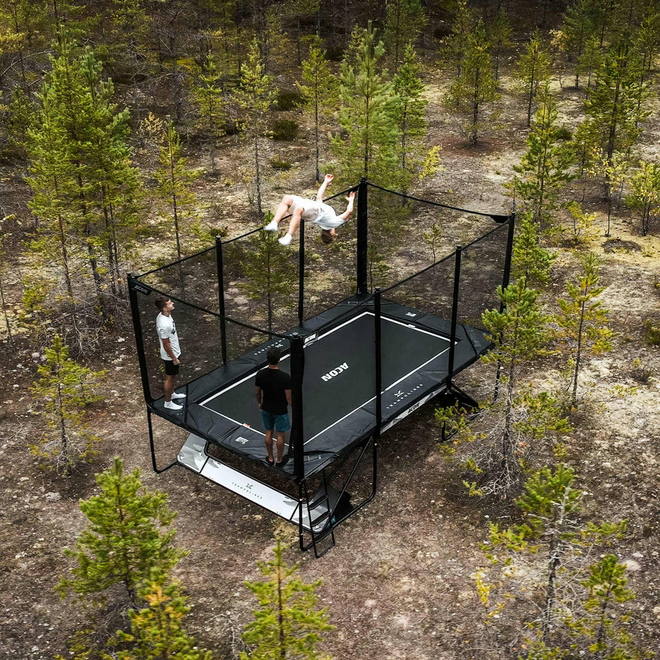 Advanced trampoline athletes performing skills on an Acon X Trampoline surrounded by scenic Nordic woodland, highlighting performance capabilities in natural outdoor environments.
