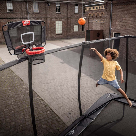 a young boy shooting ball while bouncing on a BERG trampoline with attached BERG Basketball TwinHoop accessory