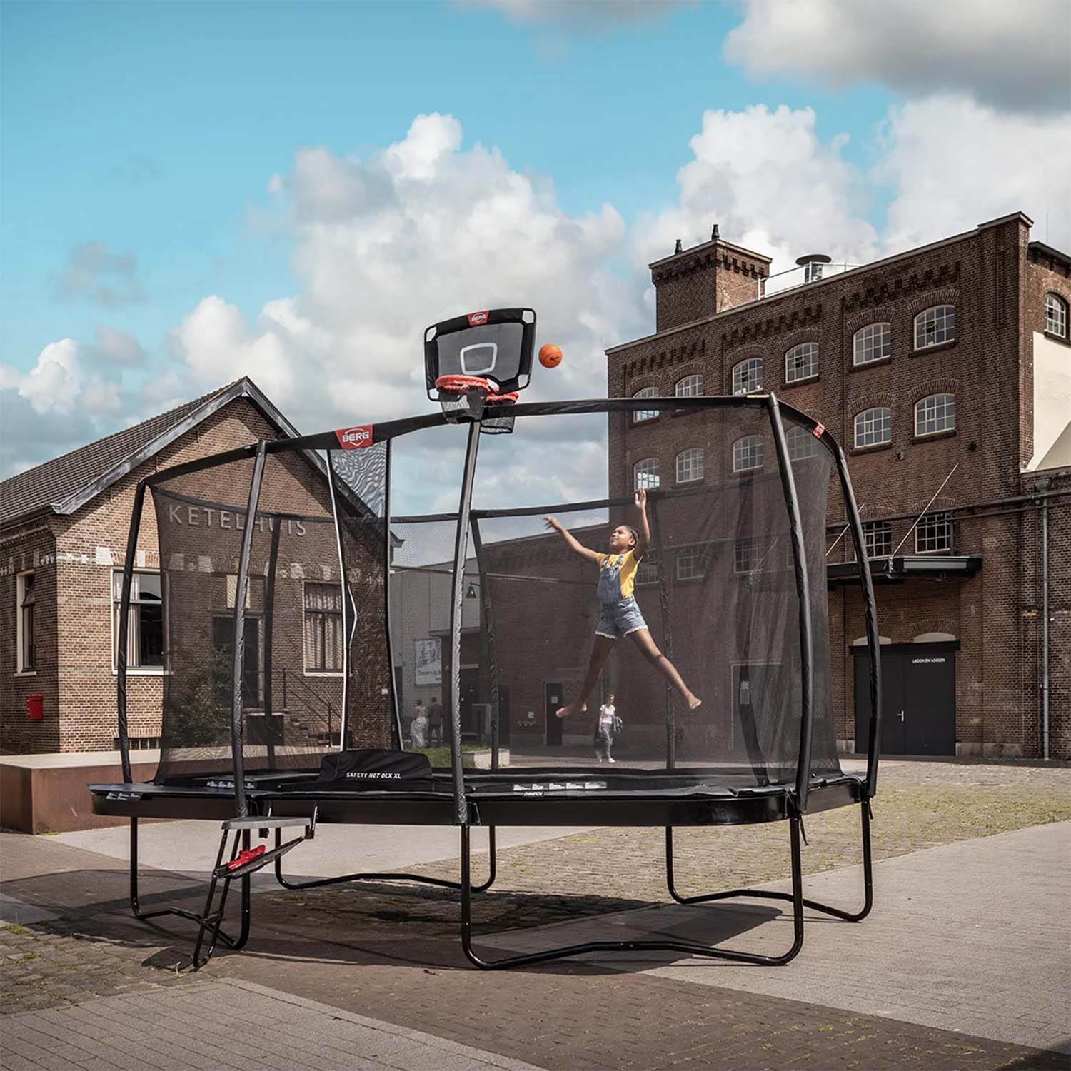 a young girl playing ball while jumping on a BERG trampoline with attached BERG Basketball Twin Hoop accessory