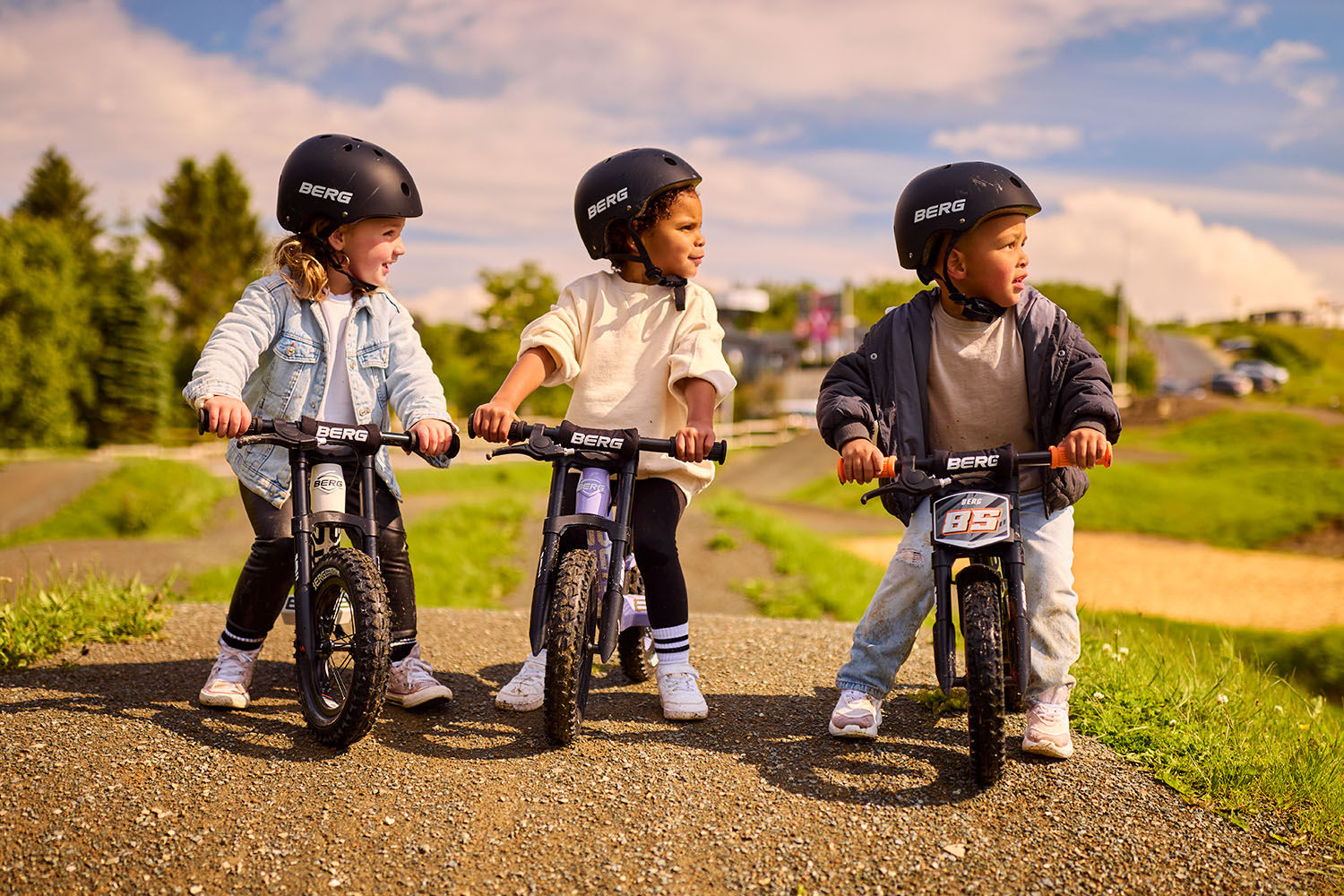 Three children riding the BERG Biky balance bike while wearing the BERG Helmet