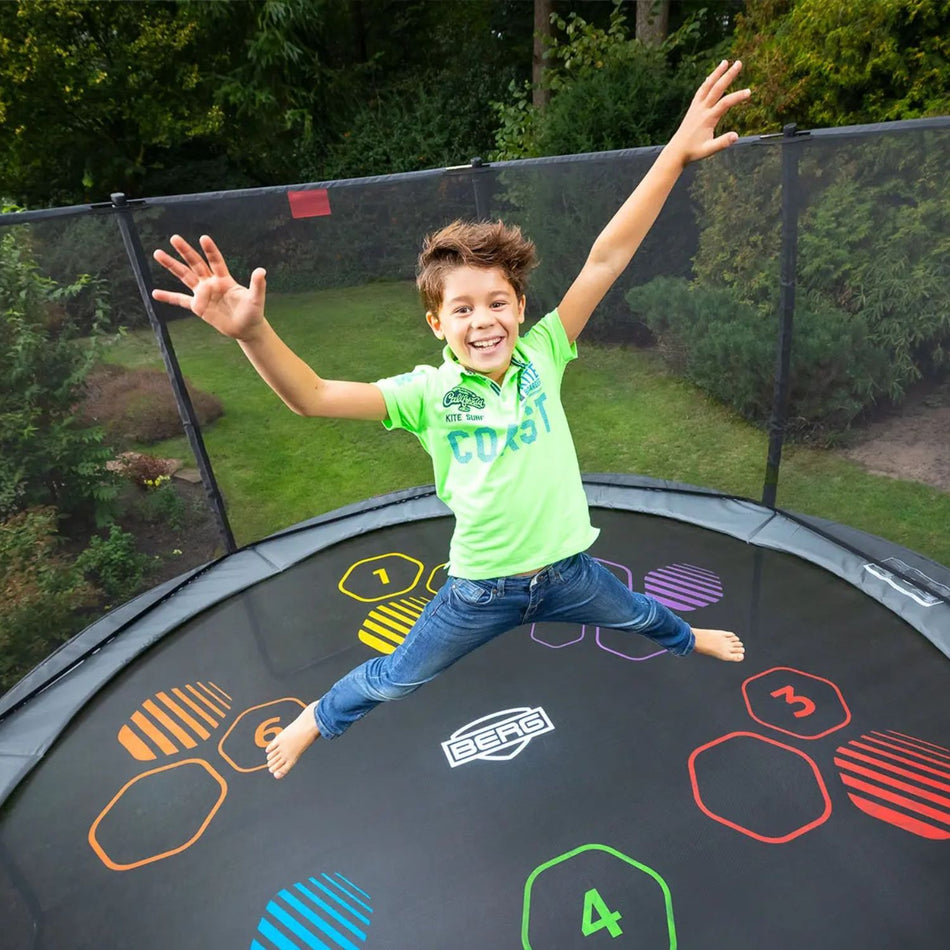 A happy boy jumping in a BERG Champion Round Trampoline with 'Levels' Jump Mat and Safety Net Deluxe in Grey colour