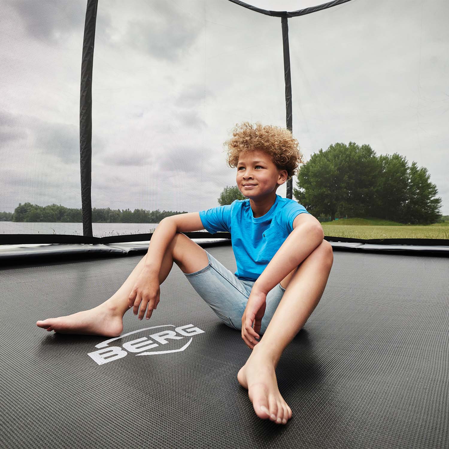 a young boy sitting in the middle of BERG Champion Trampoline with Safety Net