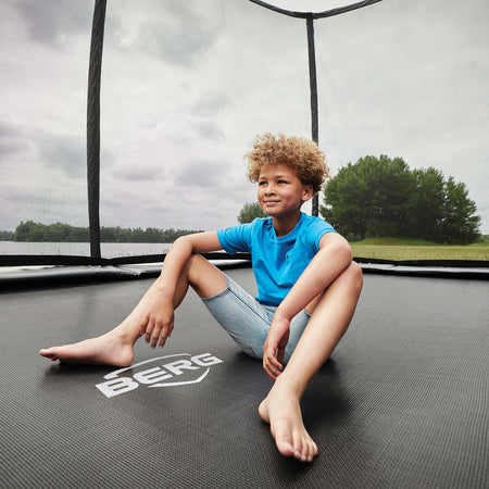 a young boy sitting in the middle of BERG Champion Trampoline with Safety Net