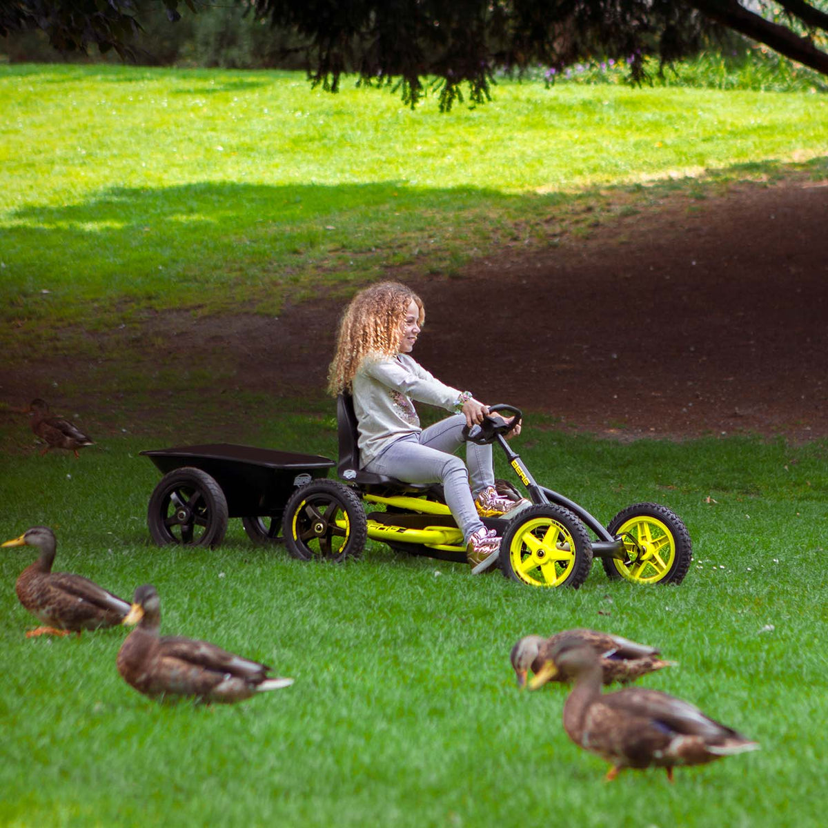 Girl playing in lawn with ducks while riding a BERG Buddy Cross with BERG Trailer Large in Black colour