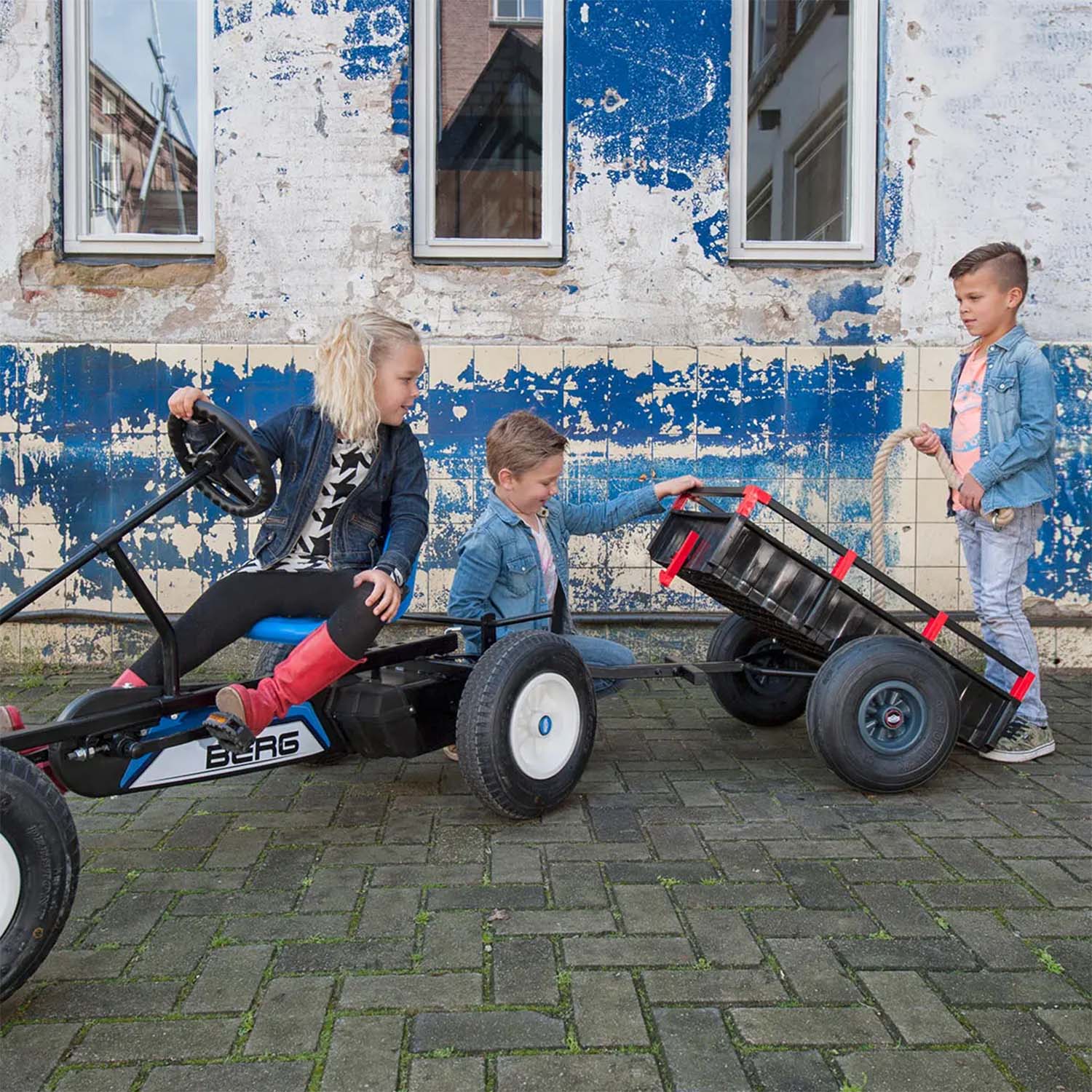 Children playing with a BERG Go-Kart with attached BERG Trailer XL accessory