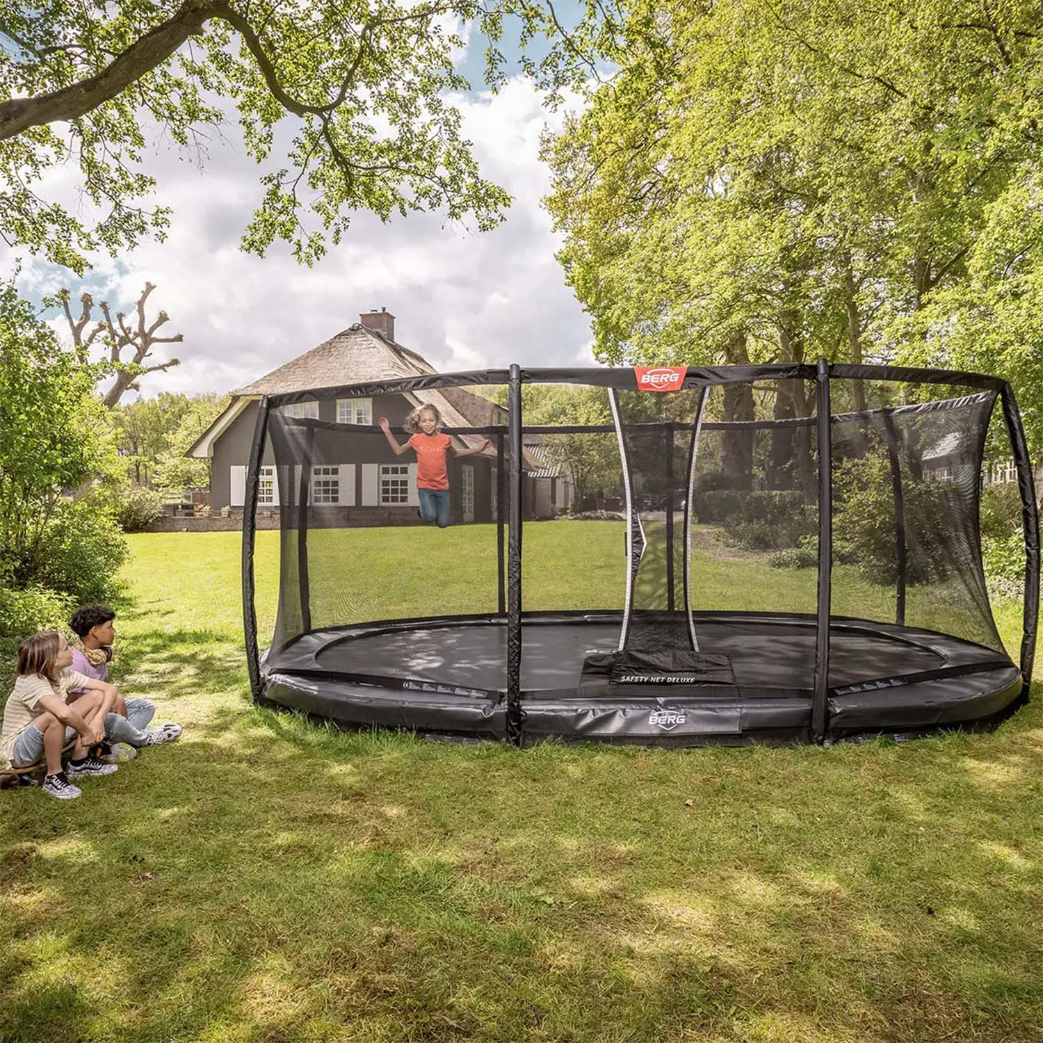 three children playing in BERG Grand Elite InGround Oval Trampoline with Safety Net Deluxe