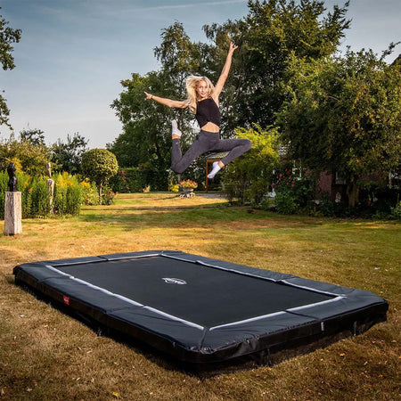 a teenage girl bouncing on a BERG SPORTS Ultim Favorit InGround Rectangular Trampoline