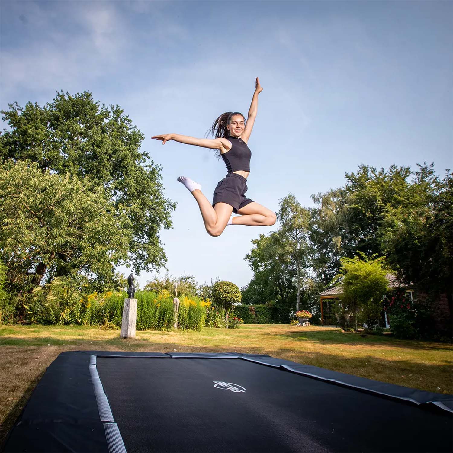 a young woman jumping on a BERG SPORTS Ultim Favorit InGround Rectangular Trampoline
