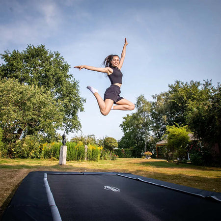 a young woman jumping on a BERG SPORTS Ultim Favorit InGround Rectangular Trampoline