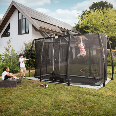 Children playing in BERG Ultim Champion ECO FlatGround Rectangular Trampoline with Safety Net DLX XL