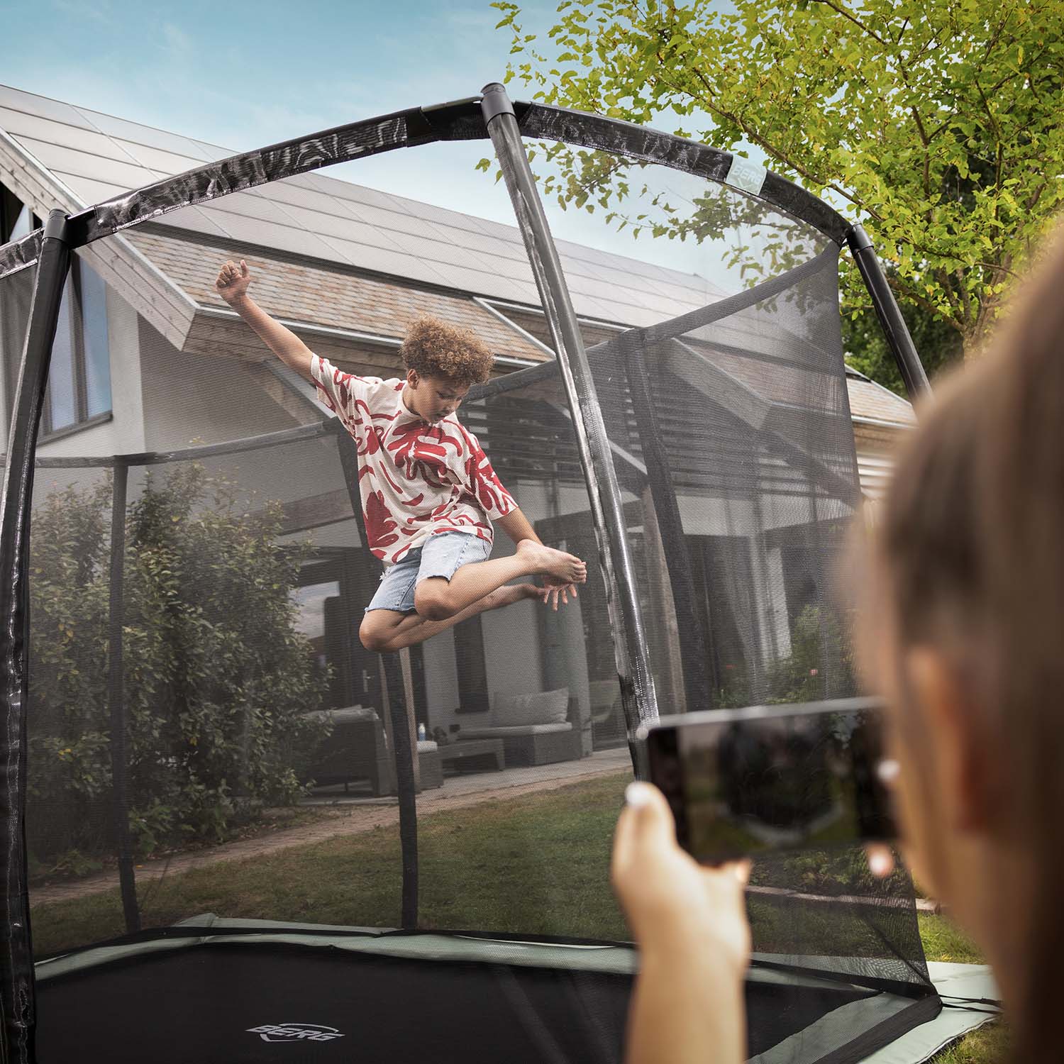 A boy jumping inside the BERG Ultim Champion ECO FlatGround Rectangular Trampoline with Safety Net DLX XL