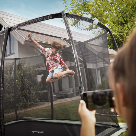 A boy jumping inside the BERG Ultim Champion ECO FlatGround Rectangular Trampoline with Safety Net DLX XL