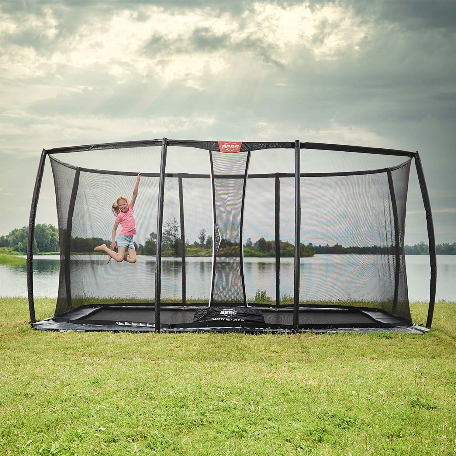 A girl playing in the BERG Ultim Champion FlatGround Rectangular Trampoline with Safety Net DLX XL
