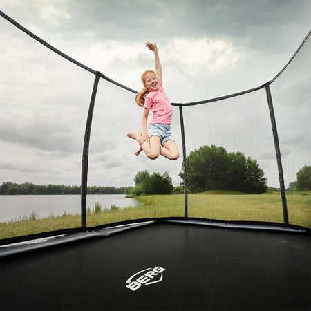 A girl happily jumping inside the BERG Ultim Champion FlatGround Rectangular Trampoline with Safety Net DLX XL