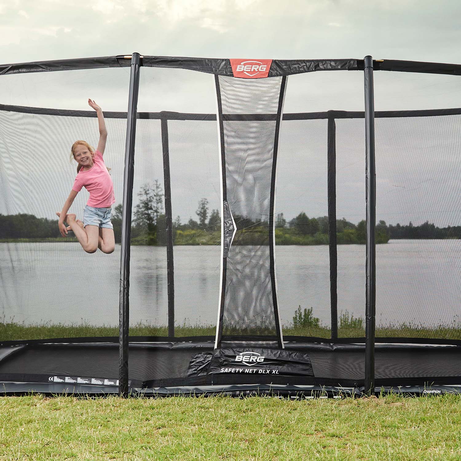 A boy having fun playing inside the BERG Ultim Champion FlatGround Rectangular Trampoline with Safety Net DLX XL