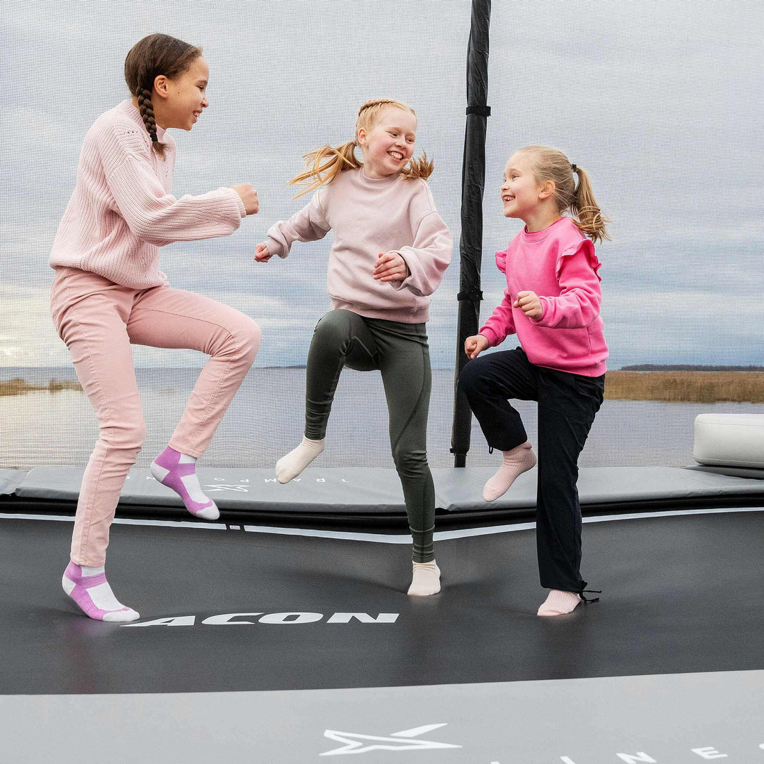 Young children in vibrant pink clothing enjoying active play time on their Acon X Trampoline, demonstrating safe recreational usage and family-friendly design.