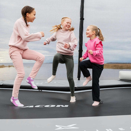 Young children in vibrant pink clothing enjoying active play time on their Acon X Trampoline, demonstrating safe recreational usage and family-friendly design.