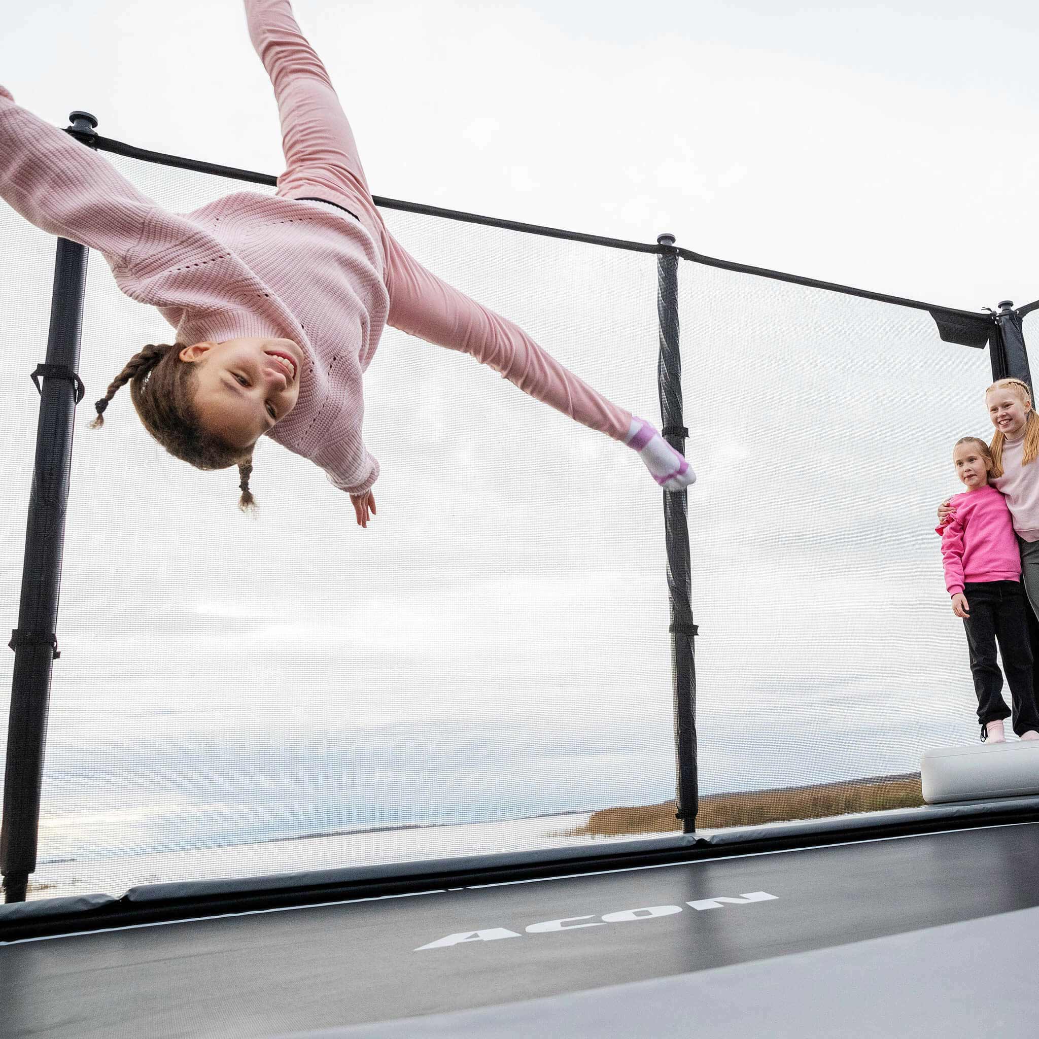 Active bouncing session on the Acon X Trampoline with one child mid-jump while friends observe safely, showcasing typical family recreation scenario and proper usage patterns.