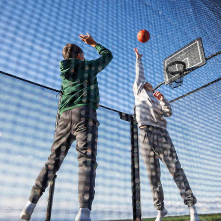 Recreational basketball activity on the Acon X Trampoline featuring young athletes combining bouncing with sport skills, demonstrating versatile entertainment possibilities.